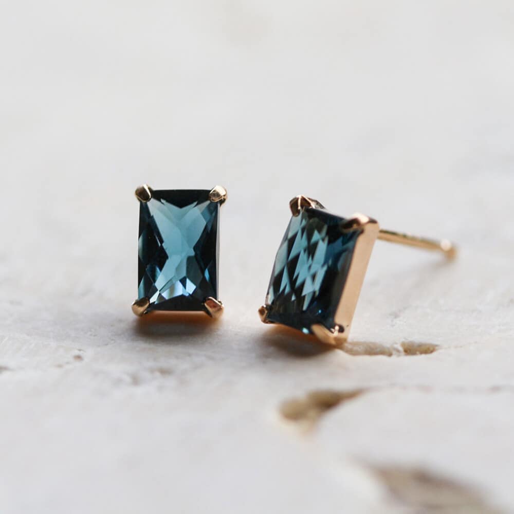 0619125027_66725583d9ad4 - SomethingBeautiful!! Blue rectangular-cut gemstone stud earrings with gold prongs on a light, textured surface.