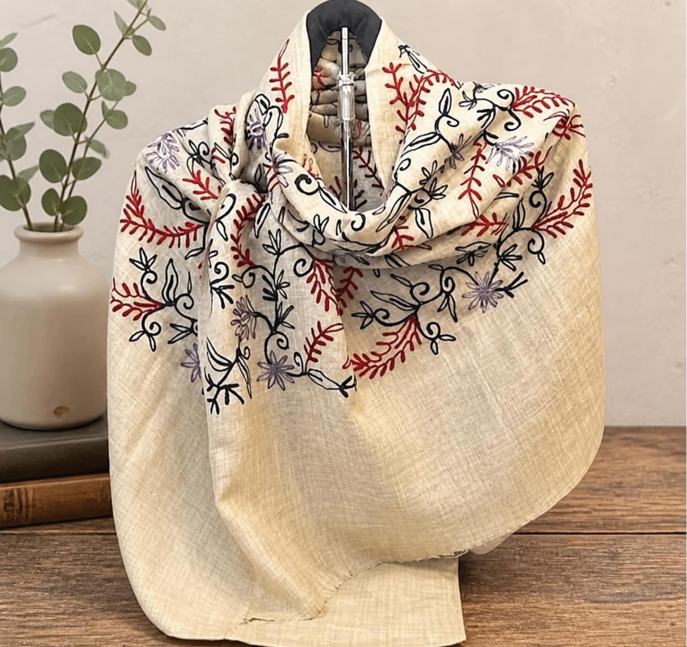 背景を変更した商品写真 - SomethingBeautiful!! Beige linen scarf with red and black floral embroidery draped over a dress form beside a ceramic vase with green stems.
