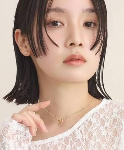 images - 2026-09-08T002938250 - SomethingBeautiful!! Close-up portrait of a woman with short black hair, wearing small earrings and a delicate gold pendant necklace over a lace top.