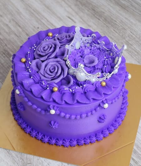 6 - SomethingBeautiful!! Purple birthday cake with piped rosettes, crown topper, and bead borders on a wooden surface.