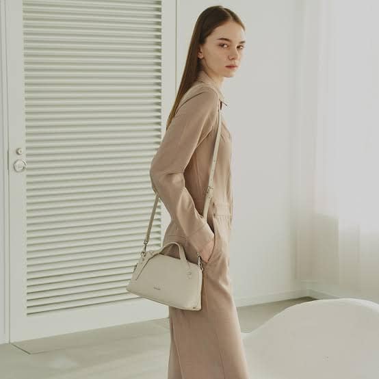 images - 2026-09-25T050937794 - SomethingBeautiful!! Woman in a beige outfit carrying a small white crossbody bag, indoors by a bright window.