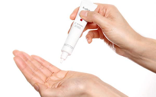img01 - SomethingBeautiful!! Close-up of hands: a person squeezing a white tube labeled 'serum' to dispense a drop onto the palm of their other hand.