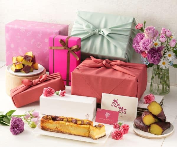 202407061946261442 1 - SomethingBeautiful!! Assorted pastel-wrapped gifts with a pink bouquet and desserts on a white table, suggesting a festive gift-giving scene.